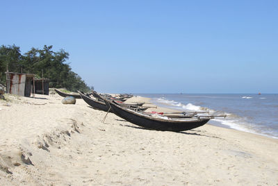 Boats moored at sandy beach on sunny day