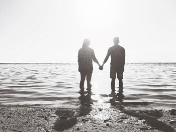 Rear view of couple walking on beach against clear sky