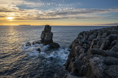 Rocks on shore against sky during sunset