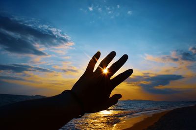 Midsection of woman at beach against sky during sunset