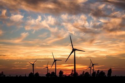 Silhouette windmills against sky during sunset