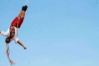 Low angle view of man hanging upside down against clear sky