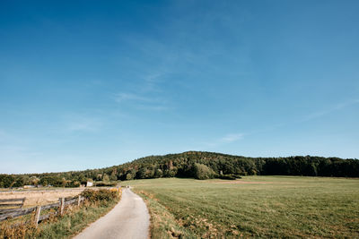 Empty road amidst field against sky