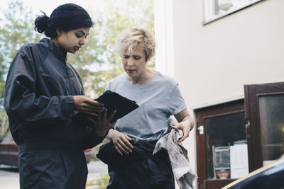 Female mechanic explaining customer over digital tablet outside repair shop