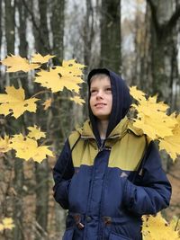 Boy looks fascinatingly standing on a background of autumn forest and yellow maple leaves