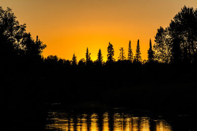 Scenic view of lake by silhouette trees against sky during sunset