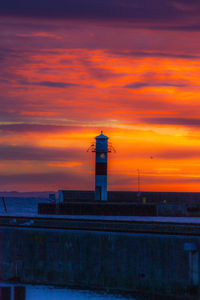 Lighthouse by sea against sky during sunset