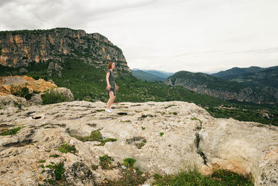 Low angle view of young woman standing on mountain against cloudy sky