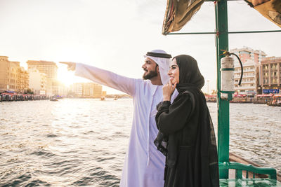 Smiling couple looking at view while standing in boat on river during sunset