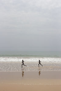 Boys running on beach against sky