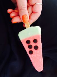 Close-up of hand holding popsicle against black background