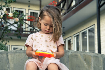 Portrait of concentrated cute little girl playing popit toy  in the yard of a small guest house.