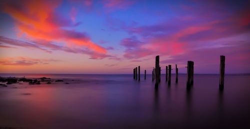 Silhouette poles in calm sea against scenic sky