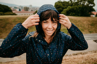 Smiling young woman with raincoat against field