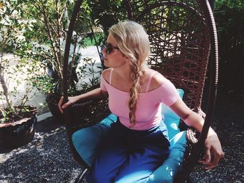 Woman wearing sunglasses sitting on swing at backyard