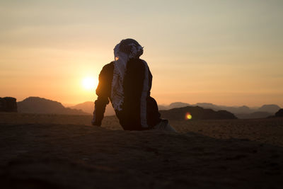 Rear view of woman standing on beach against sky during sunset