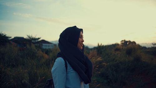 Side view of woman in headscarf standing against sky during sunset