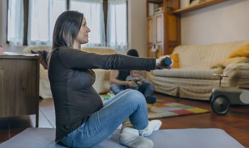 Mother exercising while father playing with son in background at home