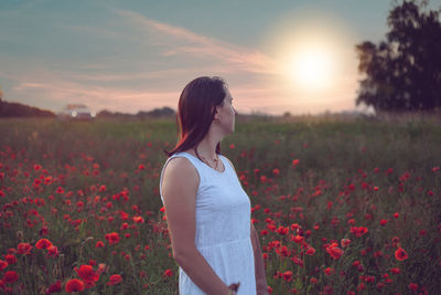 Rear view of woman standing on field against sky during sunset