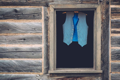 Blue waistcoat hanging on coathanger at window in log cabin