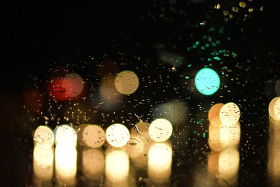 Defocused image of illuminated cars on street seen through wet glass window during monsoon