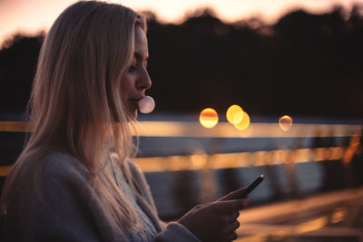 Young woman blowing bubble gum while using smart phone