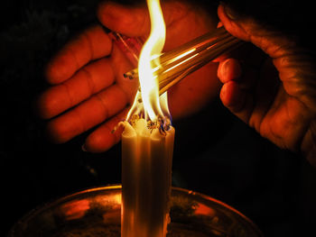 Close-up of cropped hands burning incenses from candles