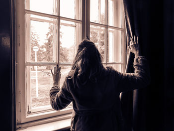 Rear view of woman standing against window