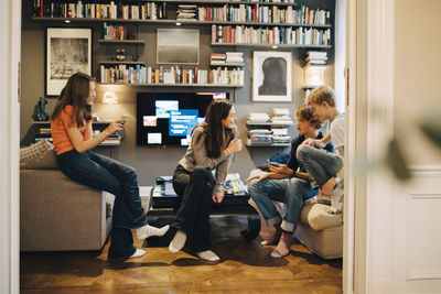 Friends talking and using mobile phone while sitting in living room at home