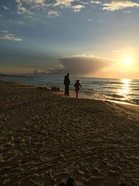 Boy standing on beach against sky during sunset