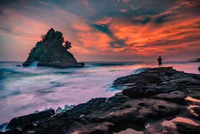 Rock formation on shore against sky during sunset