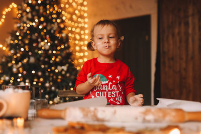 A little girl in red pajamas cooks and eats christmas cookies in the decorated kitchen of the house