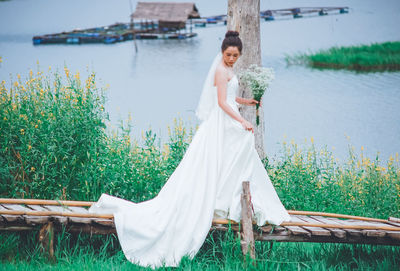 Side view of young woman holding flowers while standing on pier against lake