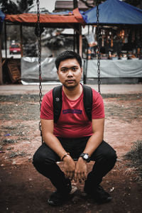 Portrait of young man sitting on swing at playground