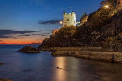 Lighthouse by sea against sky during sunset