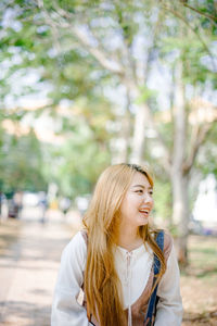 Portrait of smiling young woman against trees