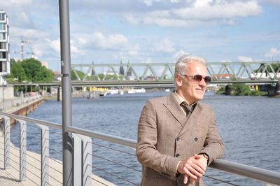 Portrait of smiling man standing on railing against river