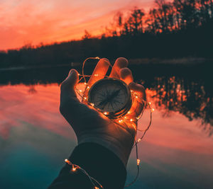 Close-up of hand holding illuminated orange against sunset sky