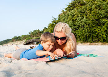 Portrait of smiling boy and woman on beach against sky