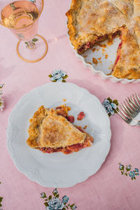 Silver forks, single slice of rhubarb pie on white plate, pink tablecloth with blue roses, rose wine