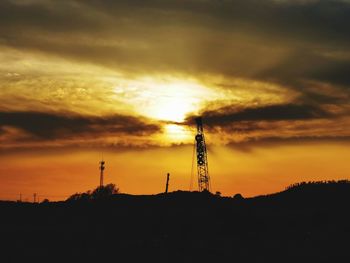 Silhouette tower and electricity pylon against dramatic sky during sunset