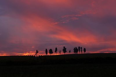 Silhouette people on field against orange sky