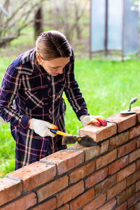 Young woman builds a wall of bricks, lays a brick on a cement-sand mortar, tapping a brick a hammer