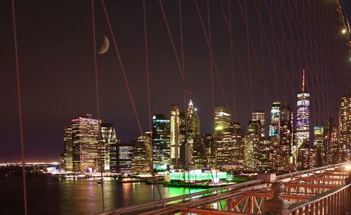 Illuminated buildings by river against sky at night