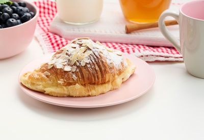 Baked croissant sprinkled with powdered sugar, blueberries on a white table, breakfast