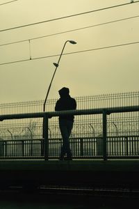 Rear view of silhouette woman standing against fence