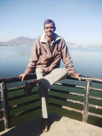 Portrait of man sitting on railing against sea