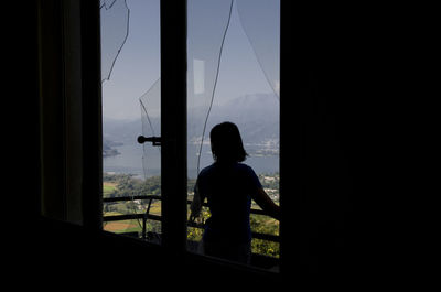 Rear view of silhouette boy looking through window