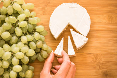 High angle view of hand holding a piece of brie cheese  on table