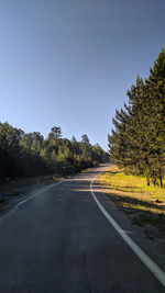 Empty road along trees and against clear sky